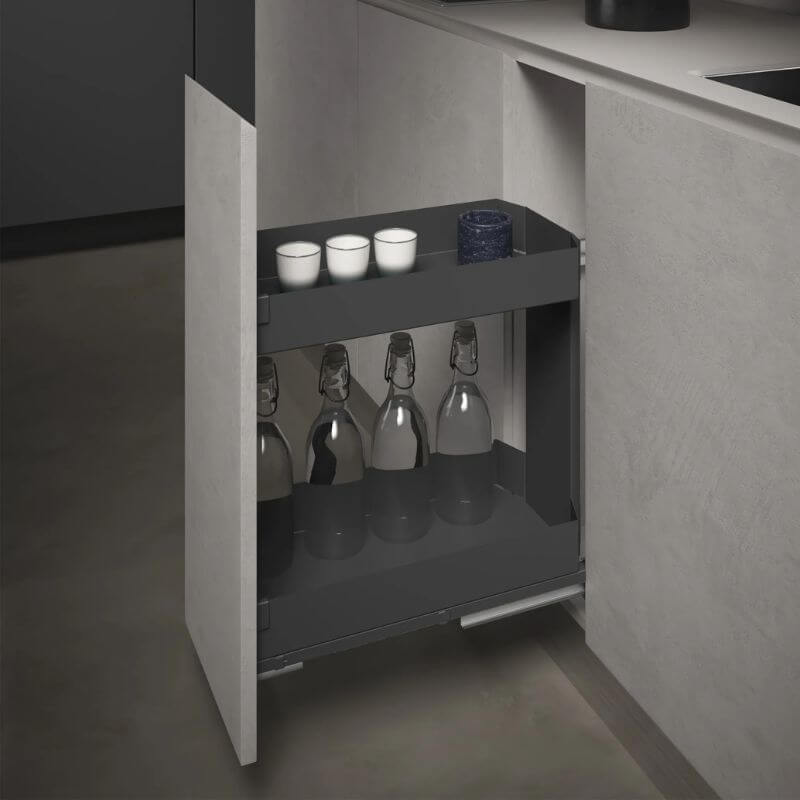 A dark gray under-counter pull-out storage cabinet shown open, holding several glass bottles and small cups, set within a modern kitchen cabinetry interior.